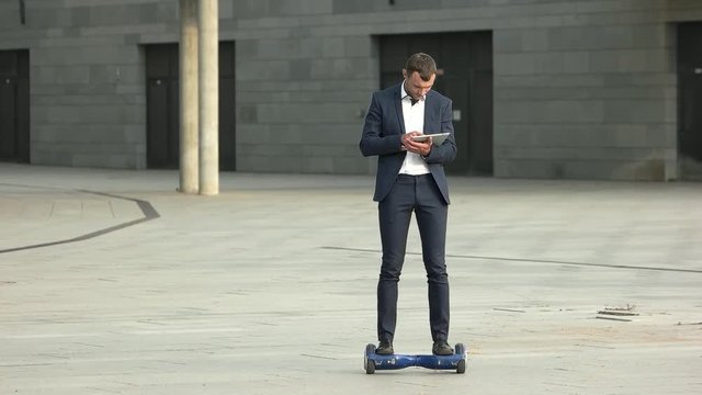 Businessman with tablet on hoverboard. Young man in the street.