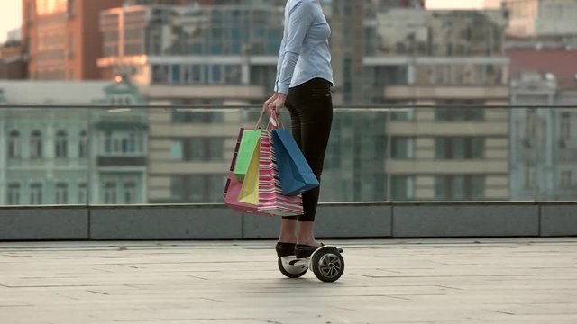 Woman with shopping bags outdoor. Hoverboard ride in slow motion.