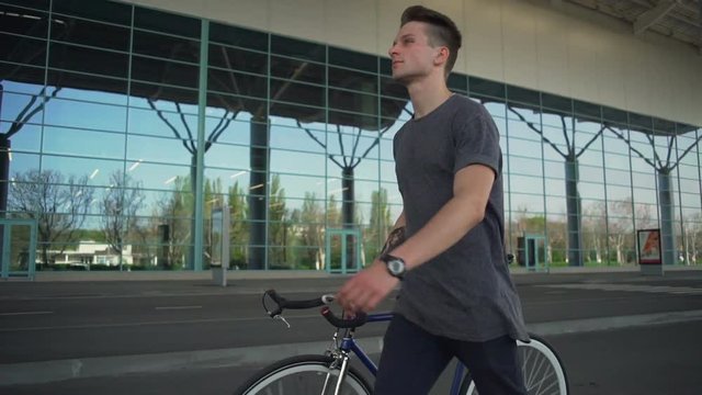 Handsome tattoed man holding his bicycle and walking slow motion