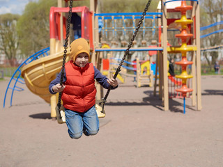 Cute European boy is swinging on children’s playground.