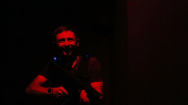Young man playing lasertag game, looking for rival in dark room, entertainment