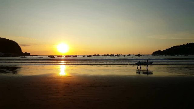 Wave surfers walking at sunset on the beach of San Juan del Sur