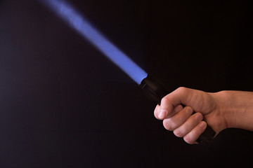 Male hand holding a led flashlight with a narrow purple beam on a black background, leaving the right side of the frame