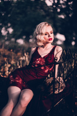 Beautiful and elegant blonde woman with red lips and hair waves wearing wine red nightie posing on...