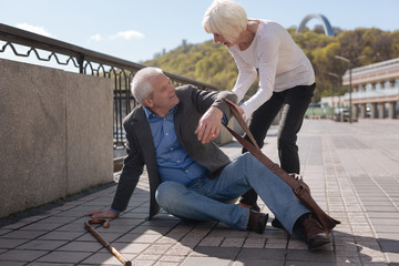 Merry pensioner sitting on the street and receiving help