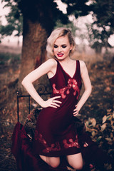 Beautiful and elegant blonde woman with red lips and hair waves wearing wine red nightie posing on...