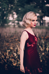 Beautiful and elegant blonde woman with red lips and hair waves wearing wine red nightie posing on...