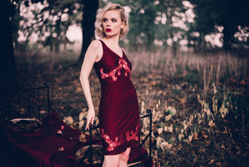 Beautiful and elegant blonde woman with red lips and hair waves wearing wine red nightie posing on...