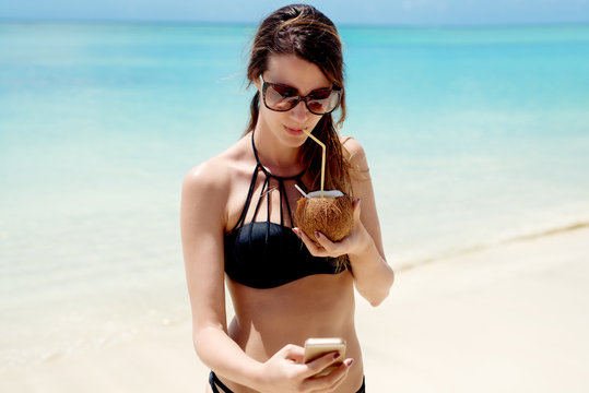 Attractive young girl drinking coconut cocktail on a beautiful beach.