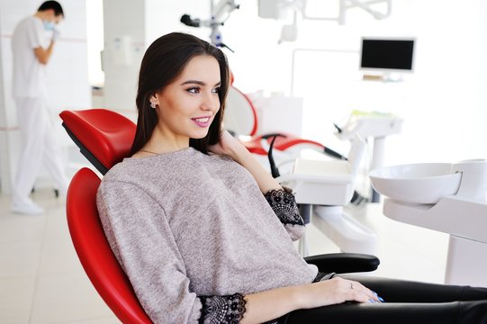 Beautiful, young brunette girl in red dental chair smiling
