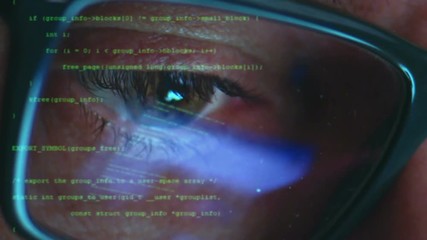 Male hacker working on a computer while green code characters reflect on his face in a dark office room
