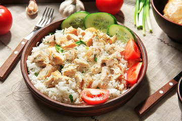 Delicious rice with chicken and vegetables in bowl on table