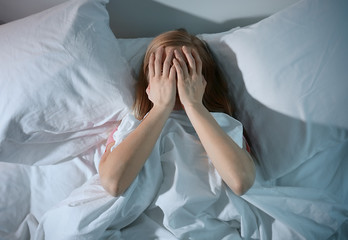 Young scared woman lying in bed at home