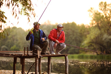 Two fishermen with fishing rods catching fish in the river standing on the pier bridge