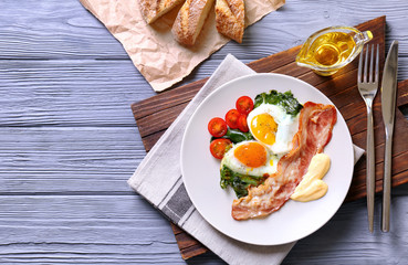 Plate with tasty eggs, spinach and bacon on wooden table