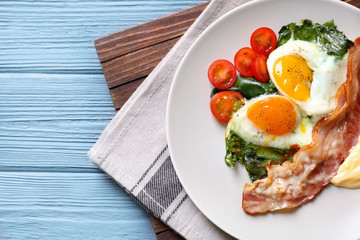 Plate with tasty eggs, spinach and bacon on wooden table