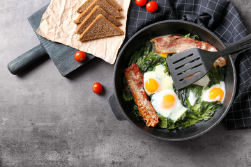 Frying pan with tasty eggs, spinach and bacon on table