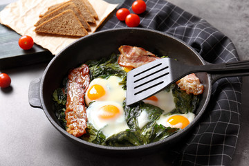 Frying pan with tasty eggs, spinach and bacon on table