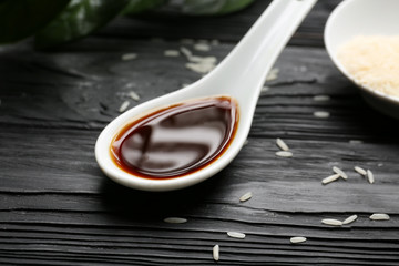 Spoon with tasty soy sauce on wooden table, closeup