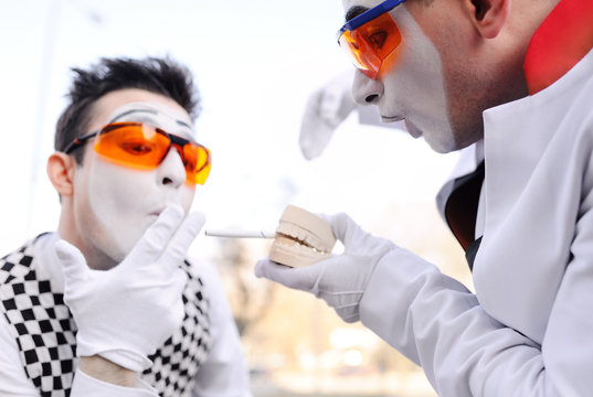 Two mimes hold in their hands an implant of the jaw with an inserted cigarette. Harm to smoking for dental health