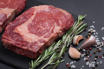 A fresh raw piece of black angus marbled meat with spices close-up on a stone dark background. Ribeye steak