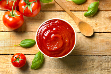 Delicious ketchup with basil and tomatoes on wooden background
