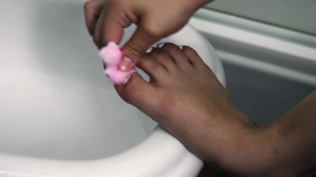 A teen aged girl removes the nail polish with a cotton in bathroom