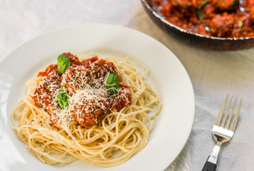 Spaghetti pasta with meatballs and cheese in tomato sauce and basil leaves against white background