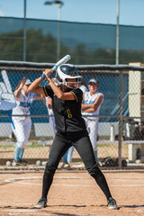 Teenage batter in black softball uniform waiting for her pitch.  