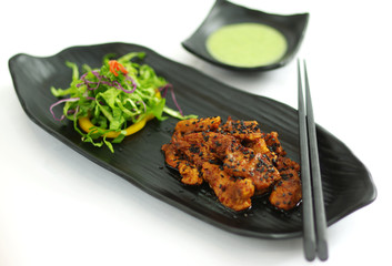 Braised pork with chili sauce, seasame and salad on black platter