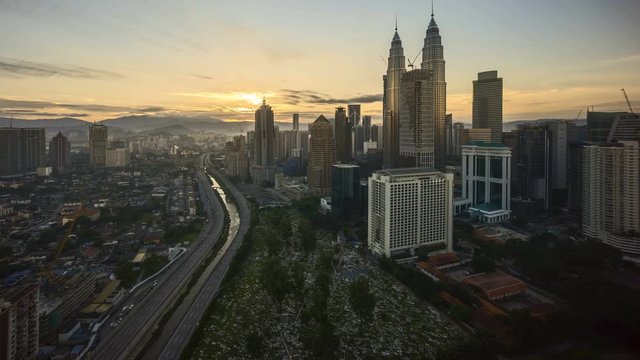 4k time lapse of dramatic sunrise at Kuala Lumpur city. Sunburst between moving clouds and building create cityscape shadow. Aerial view. Tilt up