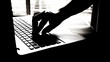silhouette black and white of anonymous hacker typing on keyboard of laptop for remotely hacking and receiving