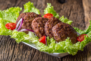 Beef Burgers meatballs cutlets with lettuce salad tomato onion on wooden board.