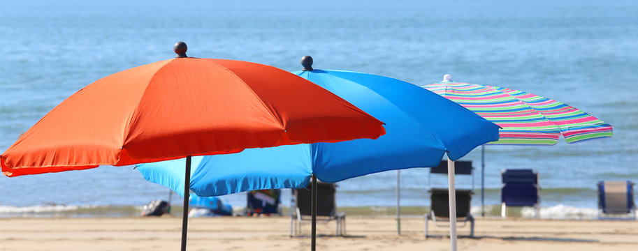 Three sun umbrellas in a row near the water of the sea on the sa