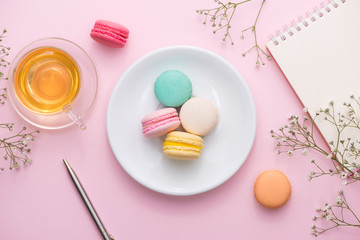 Flatlay of notebook, cake macaron, cup of tea and flower on pink table. Beautiful breakfast with macaroon.