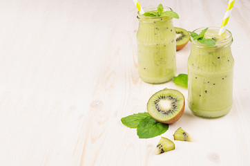 Freshly blended green kiwi fruit smoothie in glass jars with straw, mint leaf, cute ripe berry,...