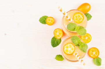 Fototapeta na wymiar Freshly blended orange citrus kumquat fruit smoothie in glass jars with straw, mint leaf, cute ripe berry, top view. White wooden board background, copy space.