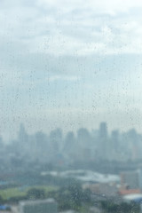 Rain drops on window glass and blurred cityscape and sunlight in background.