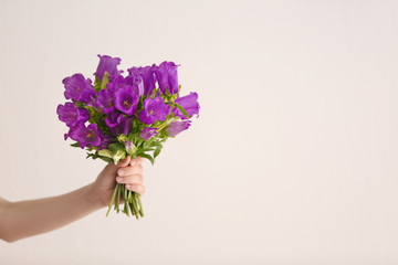 Beautiful bouquet of purple bellflowers in female hand on light background