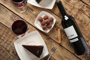 Red wine, chocolate truffles and tasty cake on wooden background
