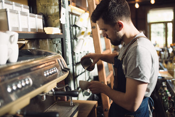 Young male barista preparing drink at coffee machine