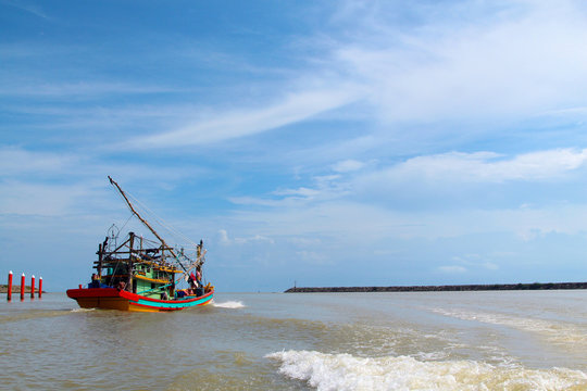 A seascape view of a fisherman fishing boat heading towards an open ocean for fishing over a blue bright sky and a cloudy day. Image shoot from a boat at Kuala Besut Jetty, Terangganu, Malaysia