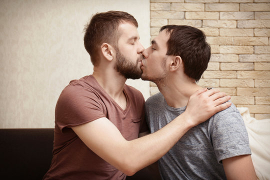 Tender kissing gay couple sitting on sofa at home