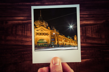 Hand holding polaroid postcard of Flinders Street Station at night. Melbourne, Australia. Travel...