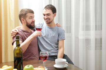 Happy gay couple drinking wine in kitchen