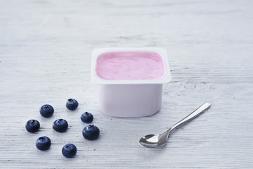 Plastic cup with yogurt and blueberries on wooden table