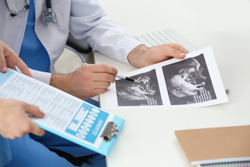 Doctor and medical assistant discussing sonogram image in office, closeup