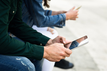 Young unrecognizable people using smartphone and tablet computers outdoors