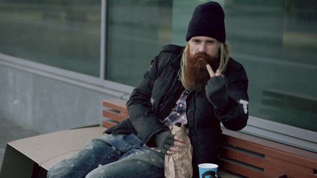 Very drunk homeless man show fuck you sign into the camera and sleeping while sitting on bench at the sidewalk