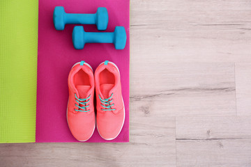 Yoga mat with sneakers and dumbbells on the floor, top view
